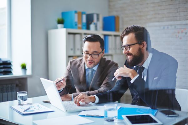 Dois homens de oculos, sentados em uma mesa apontando para a tela de um notebook, Foco no SLA e Eficiência da Telcompany